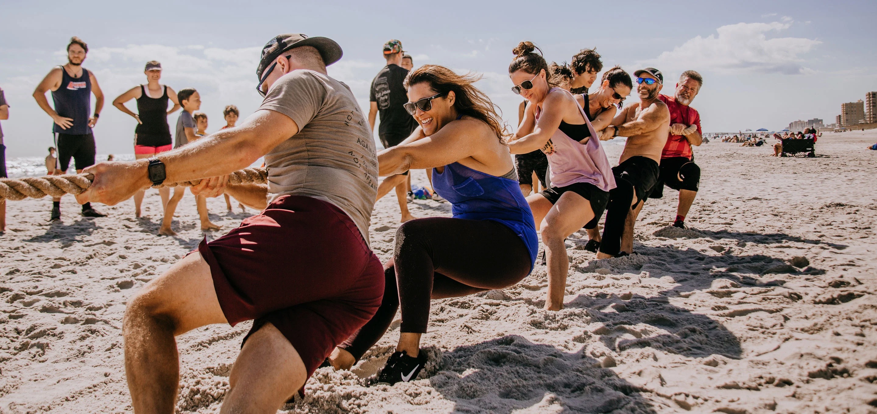 Teammates of all ages pull together on a tug-of-war rope during a beach team challenge
